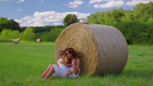Mom and daughter in white dresses in the field. Straw stacks stack bales of hay left over from harvesting crops. Landscape of straw bales against setting sun on background. High quality 4k footage - Metraje, vídeo
