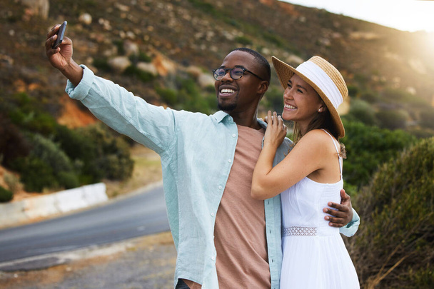 Όσο περισσότερο ταξιδεύουμε, τόσο περισσότερες αναμνήσεις κερδίζουμε. ένα ευτυχισμένο νεαρό ζευγάρι που παίρνει selfies σε ένα οδικό ταξίδι - Φωτογραφία, εικόνα