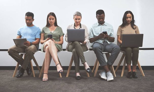 Prepare well so you can do well. a group of businesspeople using digital devices while sitting together in a line against a white wall - Foto, Bild