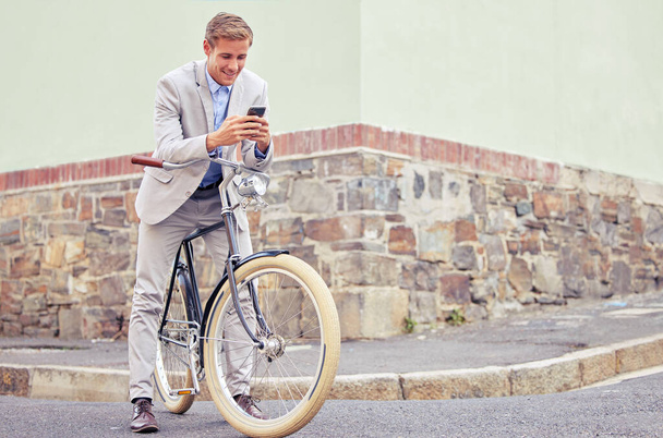 Dont ride and text. a young businessman using his smartphone while riding a bicycle - Fotó, kép