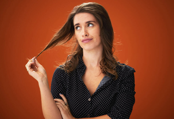Bored of this colour, its time to change. an attractive young woman standing alone against a red background in the studio and touching her hair - Foto, imagen