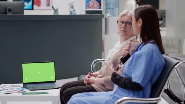 Diverse women talking about healthcare and having greenscreen on laptop in waiting room lobby. Chroma key background with isolated mockup template and blank copyspace. Tripod shot. - Materiaali, video