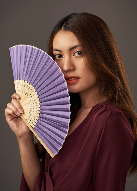 Fan the flames of beauty. Cropped portrait of an attractive young woman posing with a fan in studio against a grey background - 写真・画像