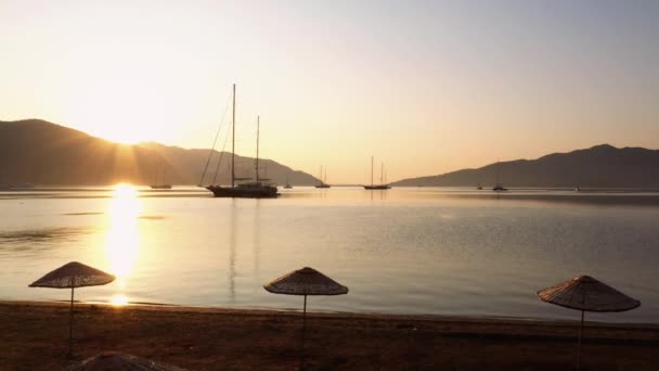 View to sea bay with sailboats from sandy beach during sunrise. The harbor in the morning with mountains in the background. - Materiał filmowy, wideo