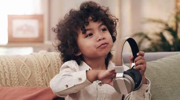 Song suggestions anyone. an adorable little boy listening to music on headphones while sitting on a sofa at home - Foto, Imagem