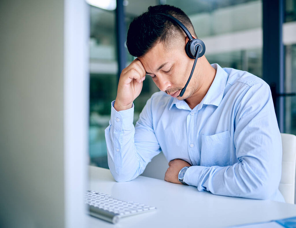 Work satisfaction is a terrible thing to waste. a young man looking stressed out while using a headset and computer in a modern office - Φωτογραφία, εικόνα