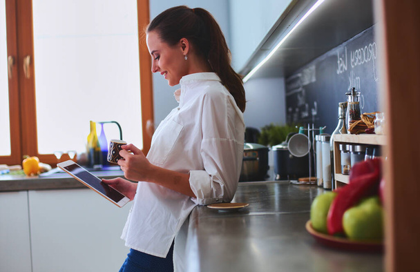 Young woman using tablet in kitchen at home and drinking coffee. - Foto, Bild