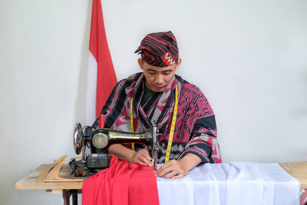  Молодий кравець у традиційному тканому одязі зайнятий тим, щоб зробити індонезійський національний прапор попереду дня незалежності. - Фото, зображення