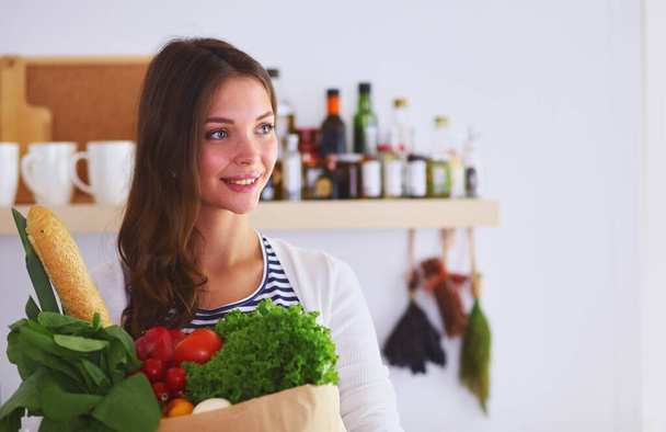 Young woman holding grocery shopping bag with vegetables .Standing in the kitchen. Young woman. - Фото, зображення