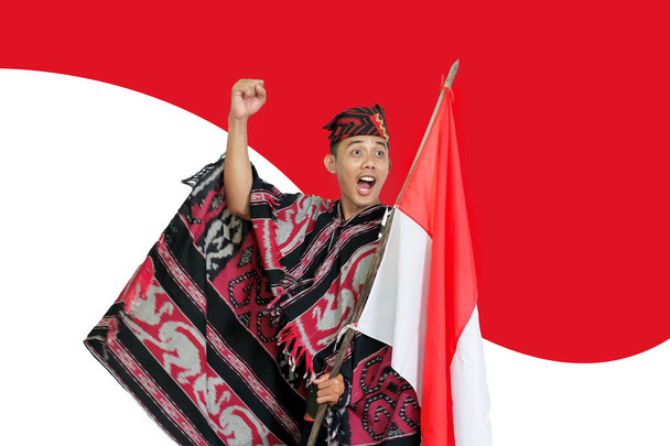 Man wearing traditional woven clothes holding Indonesian national flag in independence month with clipping path for objects and shadows, infinite depth of field - Zdjęcie, obraz