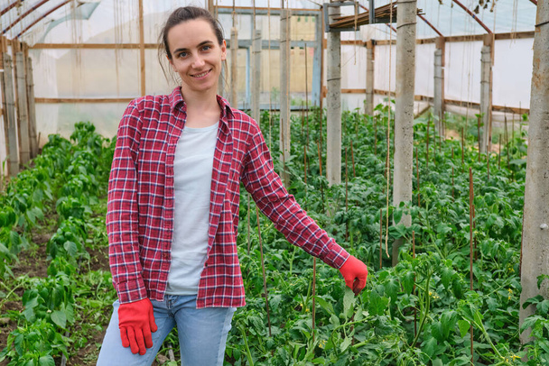 pretty female nursery worker with red Work Gloves portrait in greenhouse. High quality photo - Фото, изображение