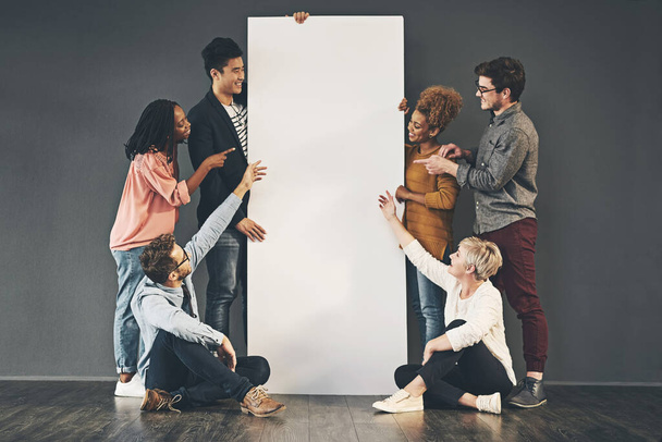 A diverse group of people holding a blank white board or poster and showing advertising copy space. A team or friends marketing a placard banner standing and sitting together for a promotion. - Photo, image