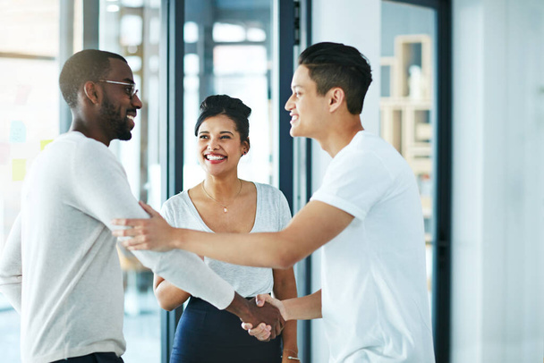Handshake, teamwork and agreement of business people greeting in an office or working together. Group or team of young colleagues talking, smiling and happy about success, a deal or promotion at work. - Foto, Imagem