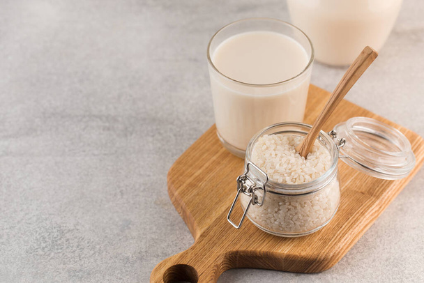  A jar of raw rice and rice milk in a glass on a plank on a gray background. Healthy food concept, alternative milk. Copy space - Photo, Image
