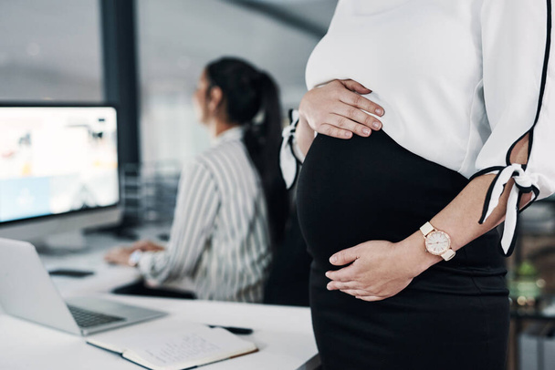 Motherhood wont stop me reaching goals. an unrecognizable pregnant businesswoman standing and holding her stomach while a colleague works behind her - Valokuva, kuva