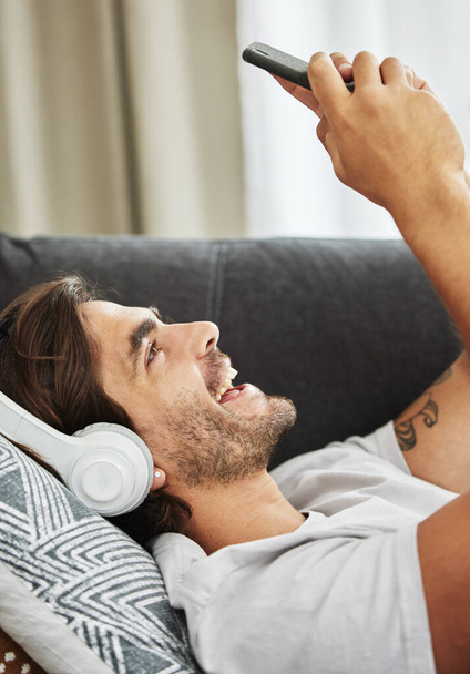 My gym sessions are about to get a lot better. a young man happily listening to music on his phone while relaxing on his sofa - Фото, изображение