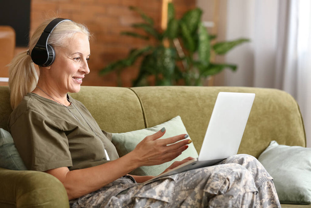 Mature female soldier in headphones using laptop at home - Zdjęcie, obraz