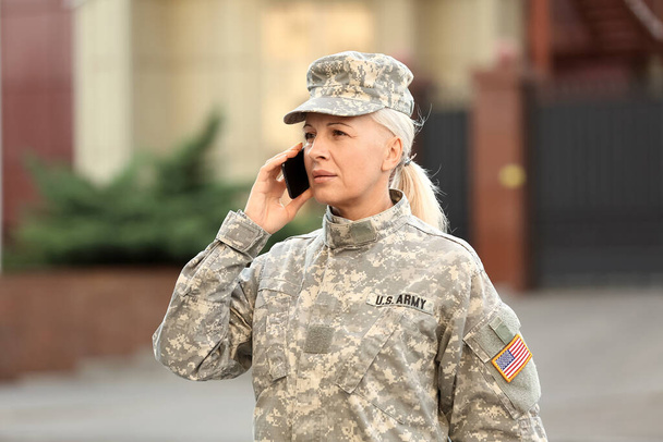 Mature female soldier talking by mobile phone outdoors - Foto, afbeelding