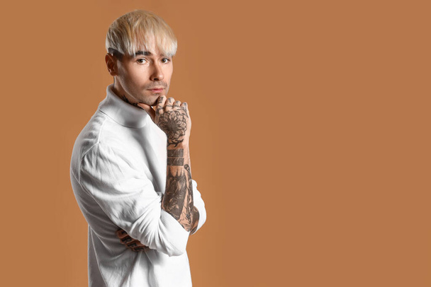 Young tattooed man in white sweater on brown background - Fotó, kép