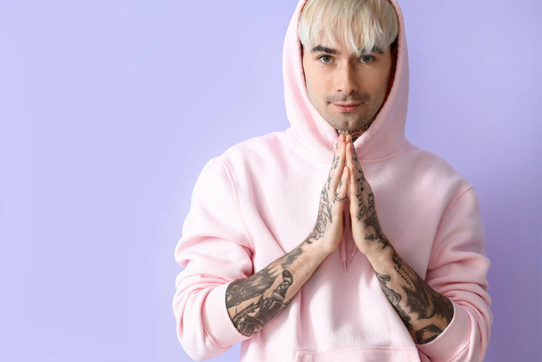 Young tattooed man in pink hoodie on lilac background - Foto, Bild