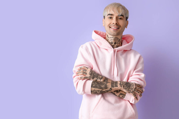Young tattooed man in pink hoodie on lilac background - Foto, imagen