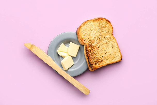 Bowl of butter, toast and knife on pink background - Foto, afbeelding