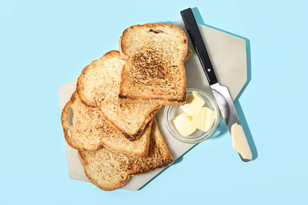 Board with toasts, bowl of butter and knife on color background - Fotografie, Obrázek