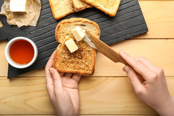 Woman spreading butter onto toast on wooden background - Foto, Imagem