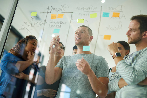 Business people brainstorming, planning and thinking of ideas on a glass board. A group or team of young professional designers using sticky notes to organize their thoughts in a modern office - Foto, imagen