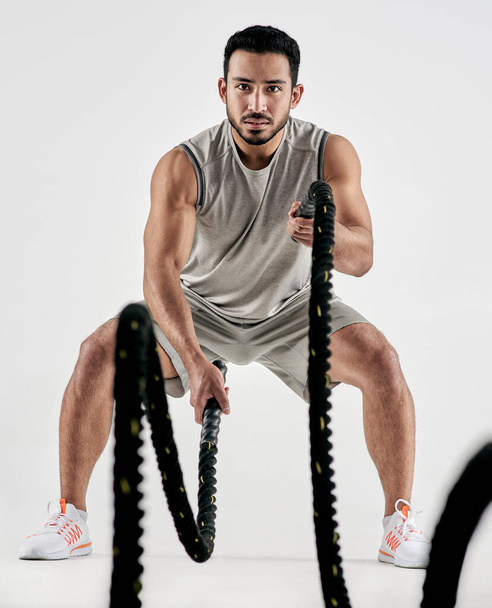 Keep calm and hiit it. Studio portrait of a muscular young man exercising with battle ropes against a white background - Photo, Image