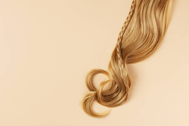 Long golden blond curly hair. A part of blond hair top view on yellow background. - Fotoğraf, Görsel
