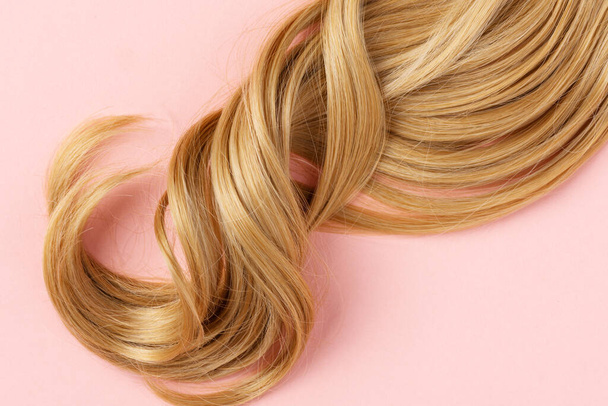 Long golden blond curly hair. A part of blond hair top view on pink background. - Fotoğraf, Görsel