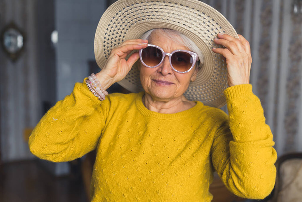 Funny caucasian senior single woman, wearing stylish sunglasses and a beach hat, having fun in retirement and getting ready for vacation. High quality photo - Foto, immagini