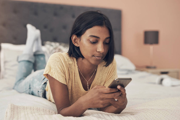 The social media streets are busier than ever before. a young woman using a smartphone while relaxing on her bed at home - Photo, Image
