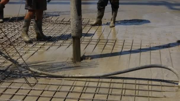 Pump hose is pouring fresh concrete in the base of new building covering square reinforcement. - Video