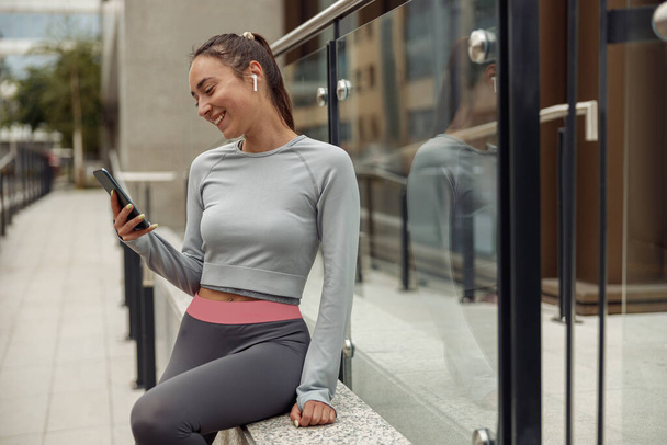 Corredor feminino conversando no telefone celular enquanto relaxa após o treinamento de fitness ativo fora - Foto, Imagem
