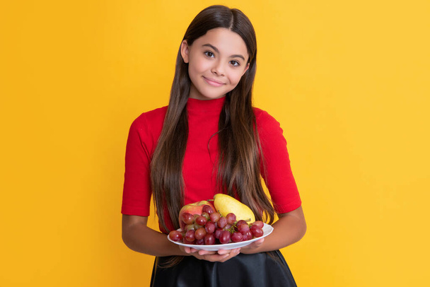 glad kid hold fresh fruit plate on yellow background. - Foto, afbeelding
