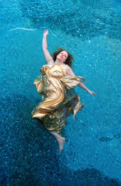 Vista superior de una hermosa pelirroja sexy sirena flota en vestido de oro como un ángel querubín en el agua, espacio de copia - Foto, imagen