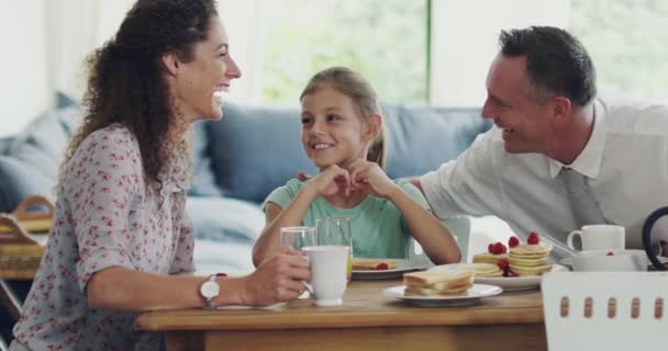 Happy family eating breakfast and enjoying the morning at home. Foster mother and father with their adopted daughter bonding, sharing and spending time together in their living room or kitchen. - Záběry, video