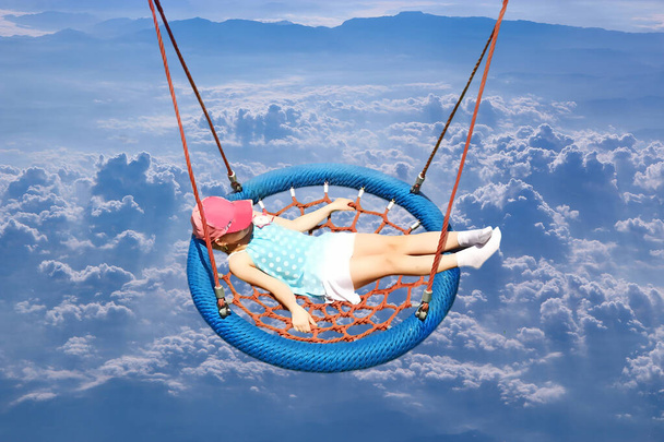 Flight over clouds.Little girl playing on swing. Happy child. Flying over white clouds. Beautiful panorama with heaven. little girl riding in hammock above clouds. Girl soars above sky - Zdjęcie, obraz