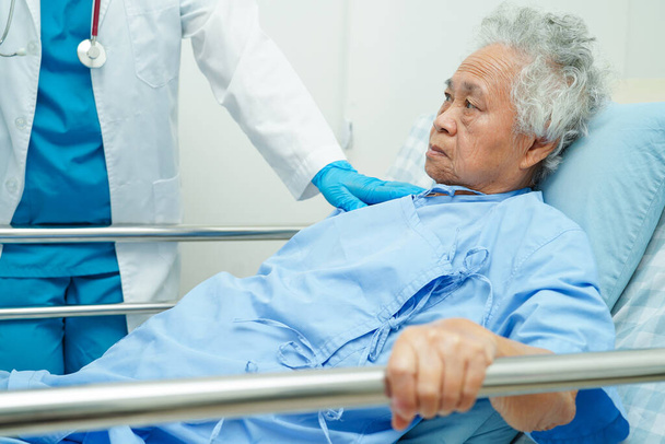 Asiatische ältere Seniorin hält Bettgitter in der Hand, während sie voller Hoffnung auf ihre Familie im Krankenhaus wartet. - Foto, Bild