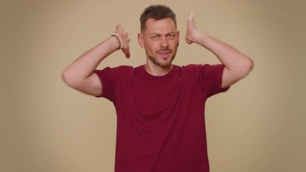 Dont want to hear and listen. Frustrated annoyed irritated handsome young man covering ears, gesturing no, avoiding advice ignoring unpleasant noise loud voices. Adult stylish guy on beige background - Záběry, video