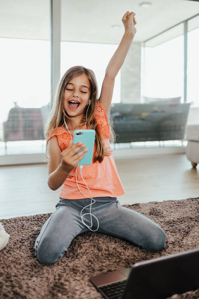Beautiful girl lies on the floor of the living room of her house and uses a laptop and smart phone for learning and communication. She is happy and smiled. - Zdjęcie, obraz