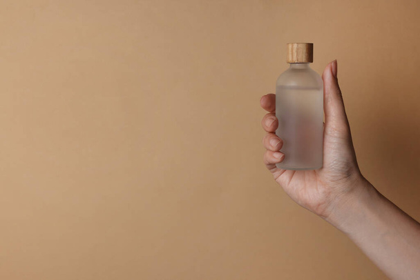 Kobieta trzymająca butelkę produktu kosmetycznego na beżowym tle, zbliżenie. Miejsce na tekst - Zdjęcie, obraz