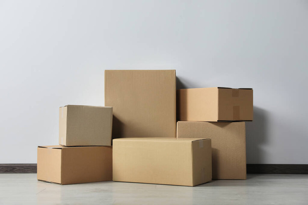 Many closed cardboard boxes on floor near white wall. Delivery service - Φωτογραφία, εικόνα