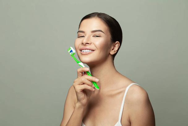 Schönheitsporträt einer glücklichen attraktiven Frau, die sich mit einer Zahnbürste die Zähne putzt, in die Kamera blickt und auf weißem Hintergrund lächelt - Foto, Bild