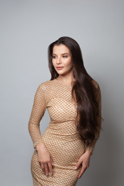 Lovely fashionable woman brunette wearing golden evening gown on white background - Zdjęcie, obraz