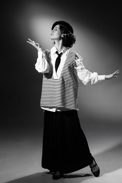 Portrait of beautiful tender woman in stylish classical clothes, striped vest and hat posing. Black and white photography. Haute couture. Elegance. Monochrome effect. Fashion, style, history concept - Photo, image