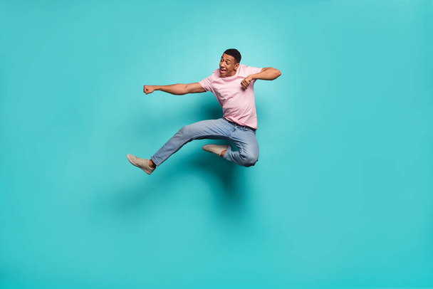 Full length photo of handsome strong guy wear pink t-shirt jumping high practicing karate isolated teal color background. - Foto, imagen