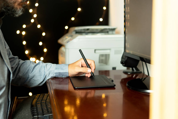 Young left-handed designer sitting at his workspace using digital graphics tablet. Working professional. Freelance. Horizontal photo. - Foto, Imagen